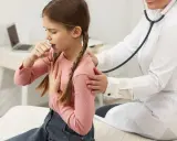 Bambina con trecce tossisce, appoggiando una mano sul petto. Un medico con camice bianco la ascolta con lo stetoscopio, preoccupato per i continui colpetti di tosse bambini.