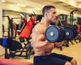 Hombre concentrado realizando ejercicios de bíceps con mancuernas en el gimnasio.