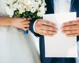 Para weselna trzyma bukiet i dokument. Na palcach widać obrączki. Co się daje na wesele? Dokumenty i kwiaty to symboliczne dary.