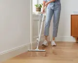 Person wischt den Holzboden, um die Wohnung zu reinigen. Ein moderner Wischmopp gleitet über das glänzende Parkett.
