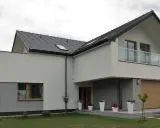 Nowoczesny dom z jasną elewacją, szarym cokołem i drewnianą bramą garażową. Idealny przykład, co na elewację domu.