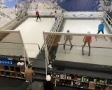 Ludzie ćwiczą jazdę na nartach na sztucznym stoku narciarskim w Ski Arenie Wrocław. Widać sprzęt narciarski i buty narciarskie w schowkach.