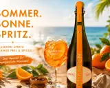Sommer, Sonne, Spritz! Ein Glas Chandon Spritz mit Orangenscheibe und Eis steht neben der Flasche am Strand. Perfekt für unvergessliche Momente.