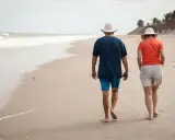 Spacerem po plaży idą emeryci. Słońce, morze i piasek tworzą idealne tło dla ich wspólnego wypoczynku.
