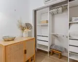 Un armario blanco organizado, listo para limpiar armarios por dentro. Cestas, ropa de cama y un jarrón con flores secas decoran el espacio.