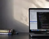 Laptop z kodem w języku C#, gdzie pętla `while` jest kluczowa. Obok leżą notatniki i ołówki.