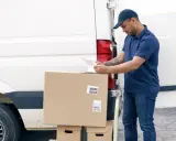 Repartidor revisa documentos junto a su furgoneta y cajas, cumpliendo la ley carga y descarga boe.