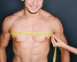 Uomo sorridente con metro da sarta al petto, per valutare se si tratta di ginecomastia o grasso.
