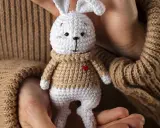 Un tierno conejito blanco con suéter tejido, parte de una colección de amigurumis originales, sostenido entre manos.