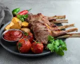 A perfectly grilled comber jagnięcy, served with roasted tomatoes, potato wedges, chili peppers, and a side of ketchup.