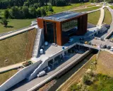 Nowoczesny budynek muzeum bitwy warszawskiej z cortenowską fasadą, otoczony zielenią i betonowymi konstrukcjami.