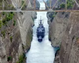 Una nave militare e un rimorchiatore navigano nel **Canale di Corinto**, tra alte pareti rocciose scavate dall'uomo.
