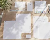Na drewnianym biurku leżą kartki papieru w formatach A4 i A3, linijka, ołówek i nożyczki. Jedna z kartek ma nadrukowany tekst i ilustracje, przypominając materiały do druku w rozmiarze papieru letter.