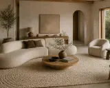 Ett lugnt, minimalistiskt hem med en böljande soffa, en rund soffbord och en fåtölj i bouclé. Naturliga material och jordnära färger skapar en harmonisk atmosfär.