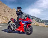 Kobieta w kasku i skórzanej kurtce przy czerwonym motocyklu Honda. Widok na góry i morze. Idealny na najszybsze motocykle na A2.