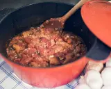 En röd gryta med en mustig toscansk tomatsoppa, en träsked rör om i den väldoftande grytan. Bredvid ligger vitlök.