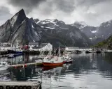 Port de pêche norvégien avec des montagnes imposantes en arrière-plan. Des bateaux de pêche sont amarrés, offrant un mouillage bateau gratuit dans ce paysage pittoresque.