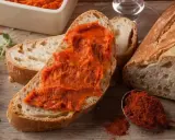 Fetta di pane con 'nduja, un assaggio di cosa mangiare in Calabria. Spezie rosse e pane fresco completano la scena.