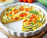Herzhafte Quiche mit Zucchini und Tomaten, garniert mit Petersilie, in einer weißen Quicheform. Ein Stück fehlt.