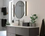 Moderno lavabo con grifería cromada, espejo ovalado y toallas negras. Ideal para una reforma de baño pequeño.