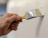 Mano aplicando pintura blanca con brocha, creando texturas. Descubre trucos para pintar paredes con efectos únicos.