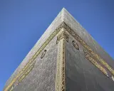 Die Kaaba in Mekka, Saudi-Arabien, mit ihrer schwarzen Hülle und goldenen Verzierungen vor blauem Himmel.