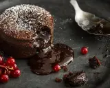 Schokoladen-Lava-Kuchen mit flüssigem Kern, bestäubt mit Puderzucker, garniert mit roten Johannisbeeren. Ein köstliches Lava Cake Rezept.