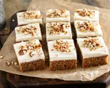 Nio bitar saftig morotskaka i långpanna med krämig frosting och hackade nötter, redo att avnjutas.