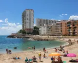 Sonniger Cullera Strand mit vielen Menschen, die sich im Meer und am Sand entspannen, im Hintergrund hohe Gebäude.
