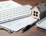 Clé, stylo, maison en bois, clavier et documents sur un bureau. Préparation de la résiliation assurance habitation.