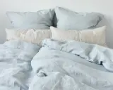 Ein Bett mit hellblauen und cremefarbenen Leinenbezügen. Perfekt für einen kühlen Sommerabend.