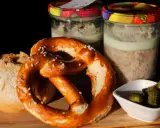 Zwei Gläser mit Fleisch einkochen im Weck-Glas, dazu ein Brezel, Brot und Gewürzgurken.
