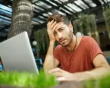 Mężczyzna z ręką na czole, sfrustrowany pracą przy laptopie. Czyżby padł ofiarą pomówienia w internecie?