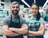 Deux employés souriants, habitués à rester debout toute la journée, posent dans un supermarché.