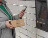 Kobieta z telefonem i paczką InPost przy automacie. Weryfikacja paczki InPost przebiega sprawnie.