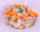 Delicioso ceviche de corvina con trozos de camote, choclo, cebolla roja y culantro, servido en un plato blanco.