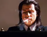John Travolta i en ikonisk scen från filmer, med rök som virvlar runt hans ansikte.