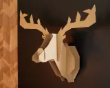 Trophée de cerf stylisé, œuvre de bricolage avec du carton de récupération, accroché sur un mur sombre à côté d'un panneau décoratif en bois.