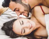 Pareja sonriente en la cama, disfrutando de intimidad.