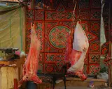 Fleisch hängt vor einem bunten Stoffmuster, bereit für Eid el Adha.