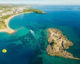 Widok z lotu ptaka na wybrzeże z hotelami, plażą i turkusową wodą. Widać łódź, parasailing i skaliste wysepki, które są świetnymi okurcalar atrakcje.