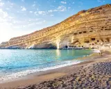 Ein malerischer Strand auf Kreta mit türkisfarbenem Wasser, das sanft an den Kiesstrand schwappt. Die beeindruckende Felswand mit ihren Höhlen bietet eine einzigartige Kulisse.