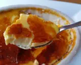 En sked lyfter en bit krämig creme brulee med knäckig karamelliserad yta.