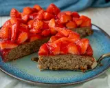 Ein saftiger, glutenfreier Erdbeerkuchen mit frischen Erdbeeren und glänzender Tortenglasur auf einem blauen Teller.