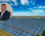 Uśmiechnięty mężczyzna w garniturze na tle farmy fotowoltaicznej. Obraz symbolizuje produkcję energii z fotowoltaiki w poszczególnych miesiącach.