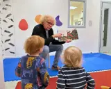 En man med lockigt hår läser en bok för två små barn. Bilden visar en humlan djojj på en morot i boken.