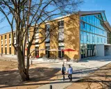 Modernes Gebäude mit Glasfront und Fassade aus nachhaltigen Materialien. Zwei Männer gehen auf einem Weg.