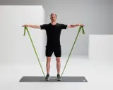 Mann trainiert mit einem grünen Widerstandsband, um seine Rotatorenmanschette zu stärken.
