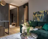 Elegancki salon w butelkowej zieleni i drewnie. Kot odpoczywa na kanapie, obok wazon z kwiatami.
