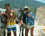 Tony Pike Ibiza: due ragazzi con asini, uno con pantaloncini colorati, l'altro con giacca di jeans e cappello di paglia, sorseggiano bevande.